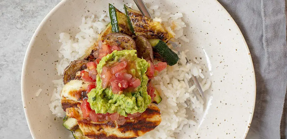 A bowl of grilled potatoes, zucchini, and halloumi on a bed of rice.