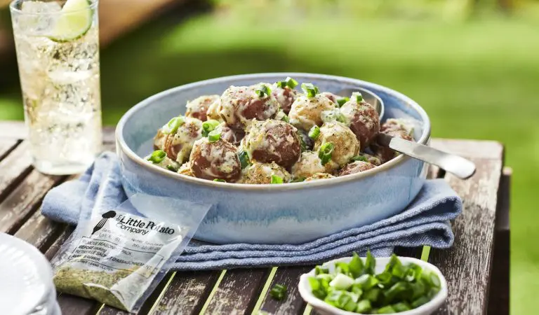 An easy to make potato salad in a blue bowl with a refreshing drink nearby.