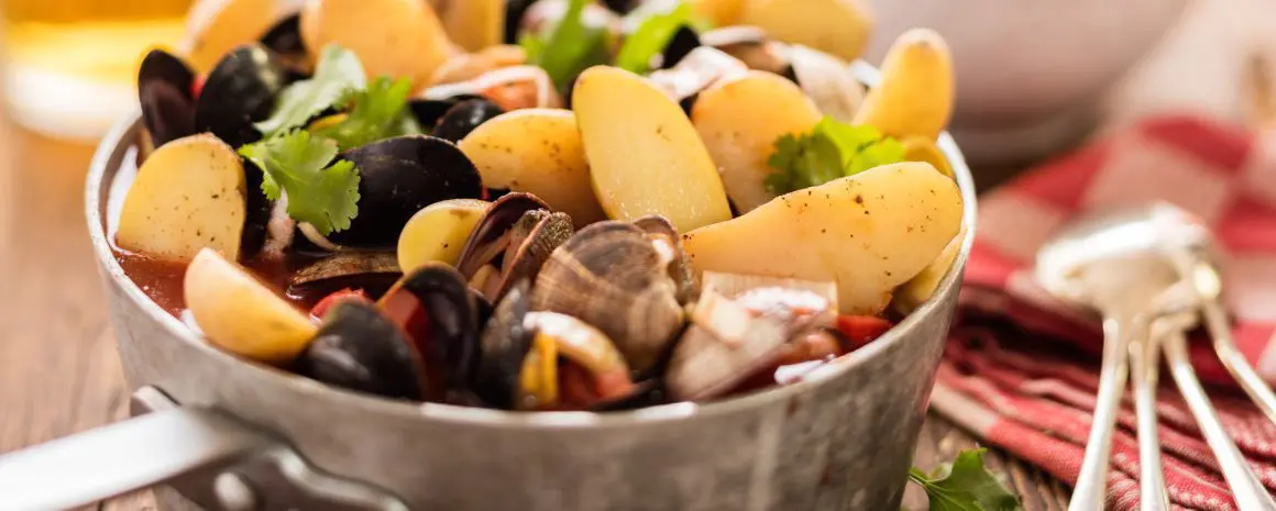 A large stock pot of seafood soup full to bursting with shellfish and potatoes.