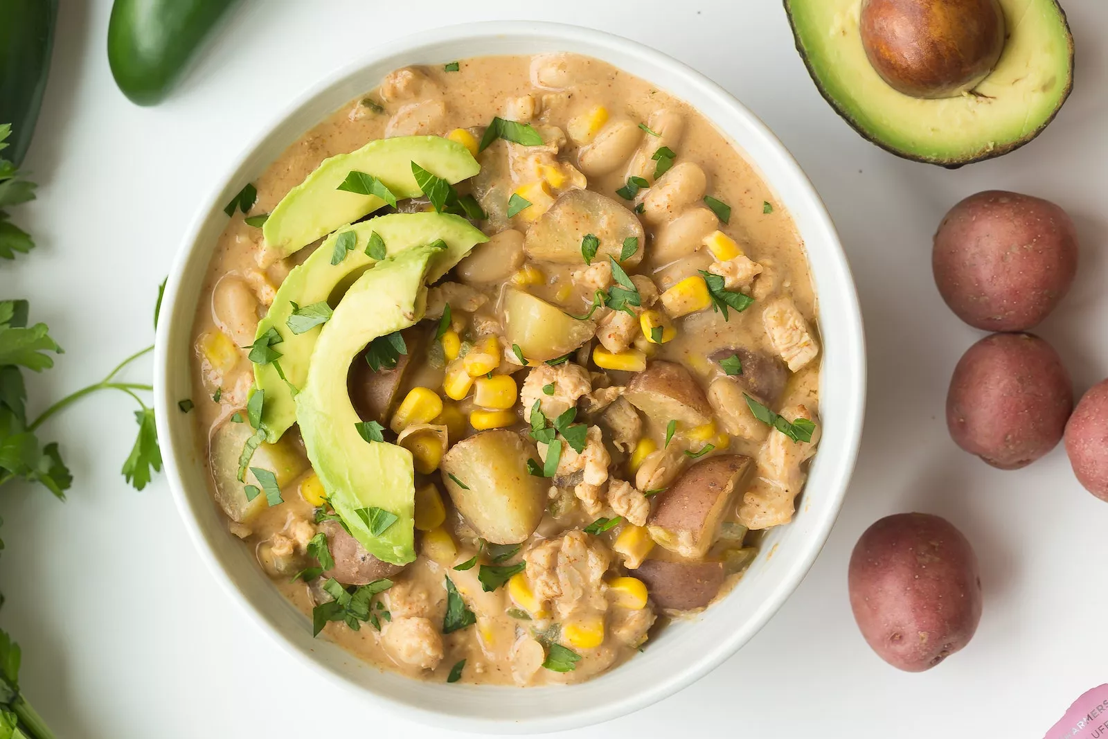 A bowl of white chili with chicken and beans and avocado.