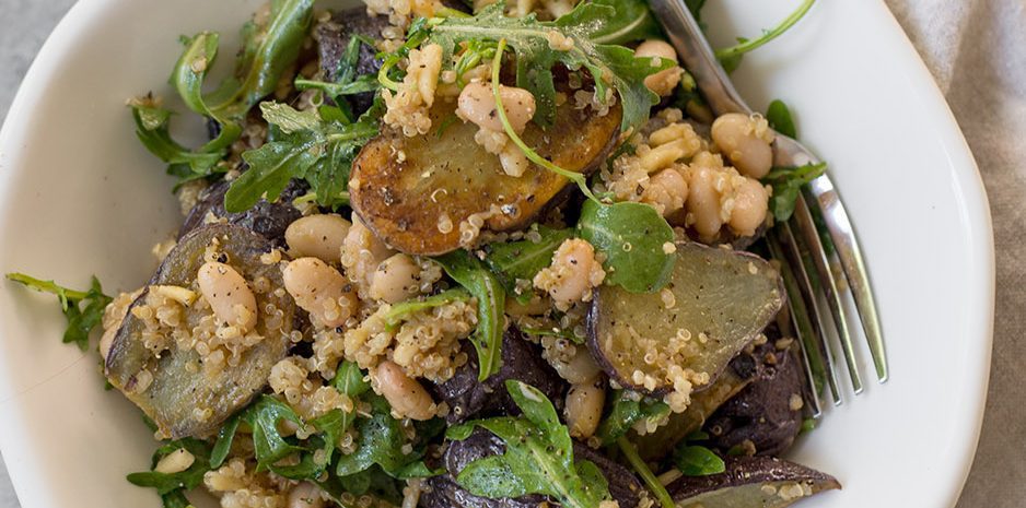 A bowl of arugula salad with white beans and little potatoes.