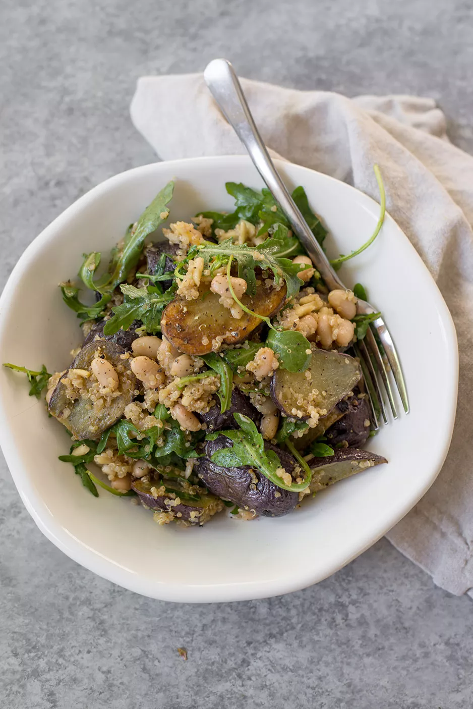 A bowl of arugula salad with white beans and little potatoes.