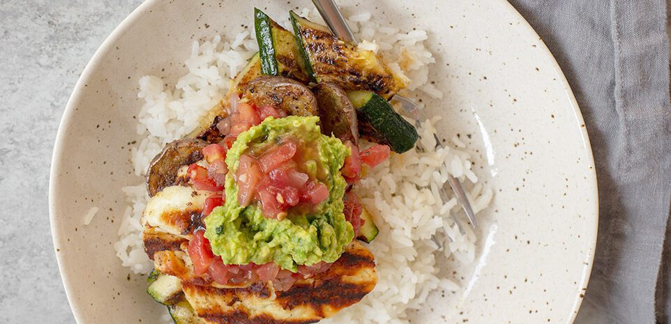 A bowl of grilled potatoes, zucchini, and halloumi on a bed of rice.