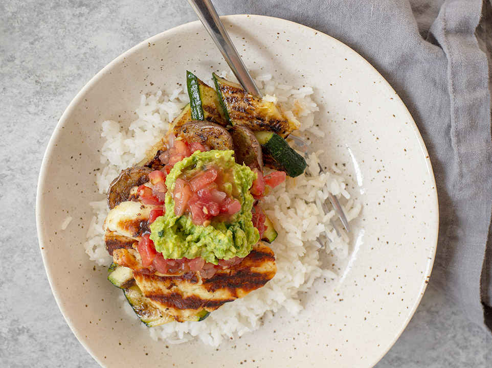 A bowl of grilled potatoes, zucchini, and halloumi on a bed of rice.
