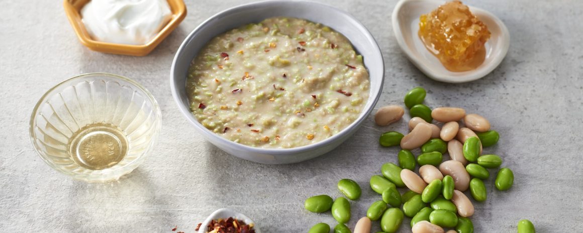 Some edamame and white bean dip with ingredients around it in a cute little bowl.