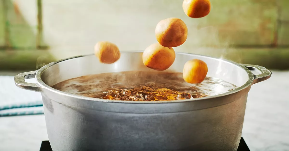 Potatoes being tossed into a pot of boiling water.