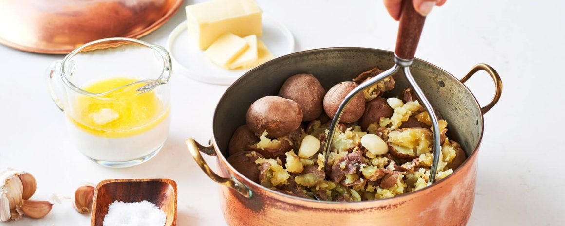 A nice big pot of boiled potatoes that are being mashed.