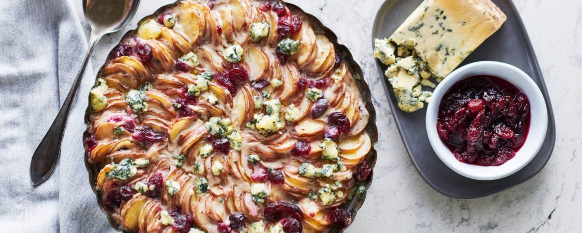 A nice pie dish full of beautifully arranged scalloped potatoes with cranberry sauce and stilton cheese on top.