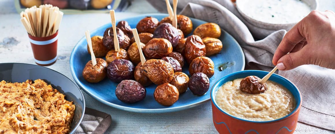 A plate of potatoes with toothpicks in them with dips on the side.