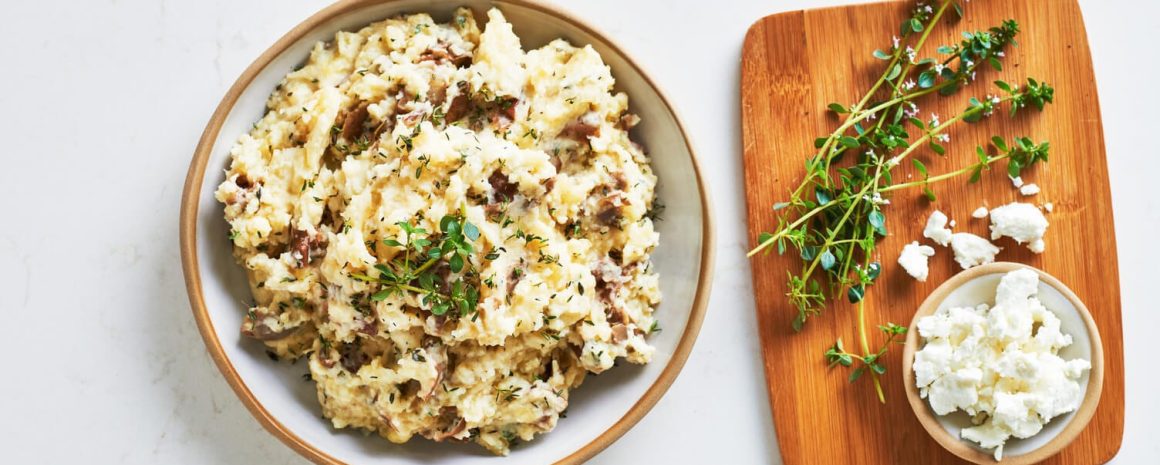 A bowl of goat cheese and thyme mashed potatoes with some sprigs of thyme nearby.