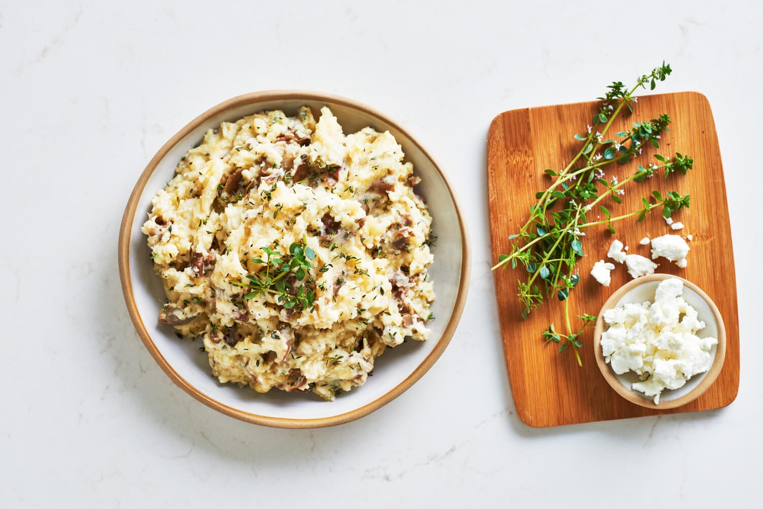 A bowl of goat cheese and thyme mashed potatoes with some sprigs of thyme nearby.