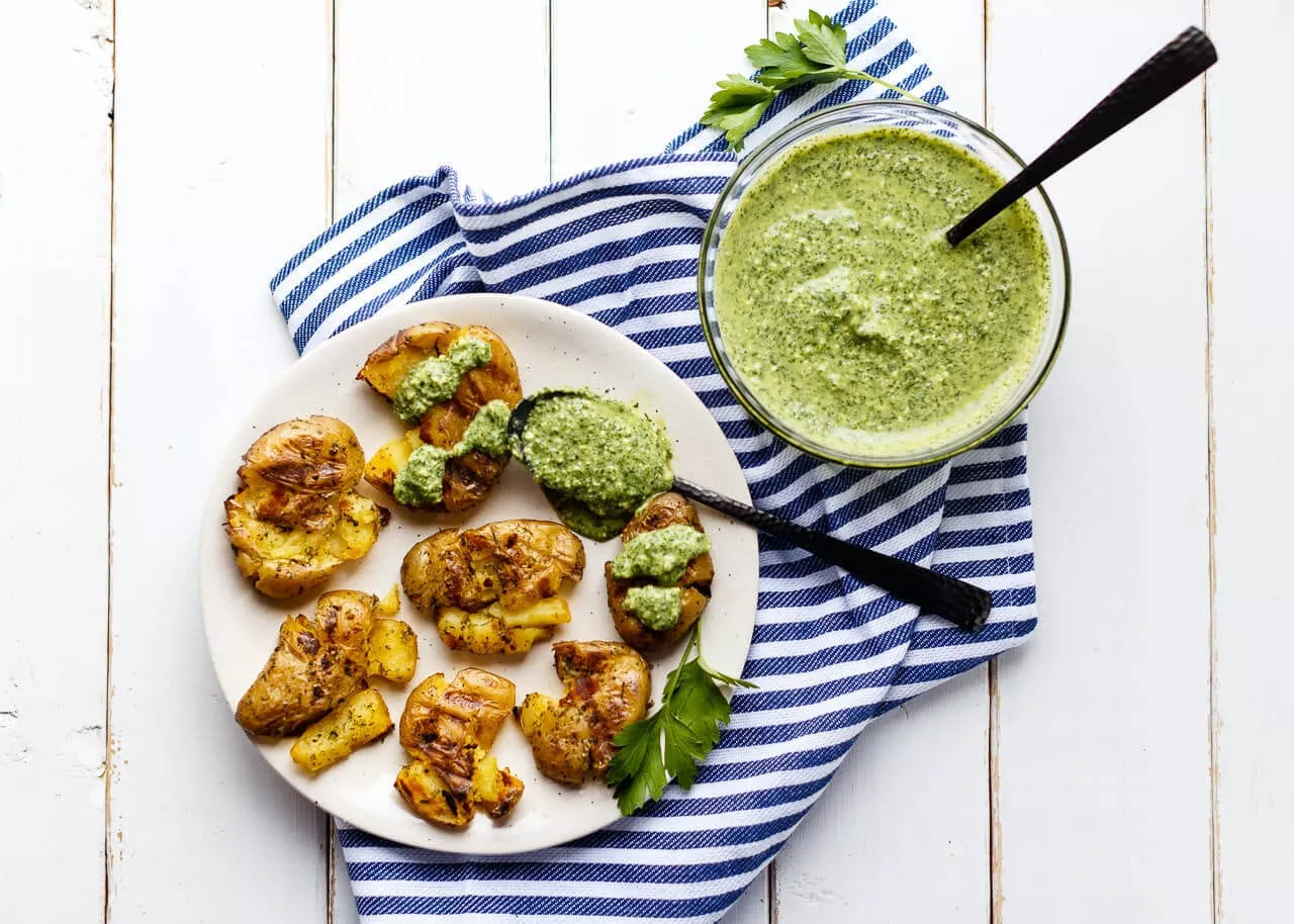 Grilled smashed fingerling potatoes on a plate with some dill dip on the side.