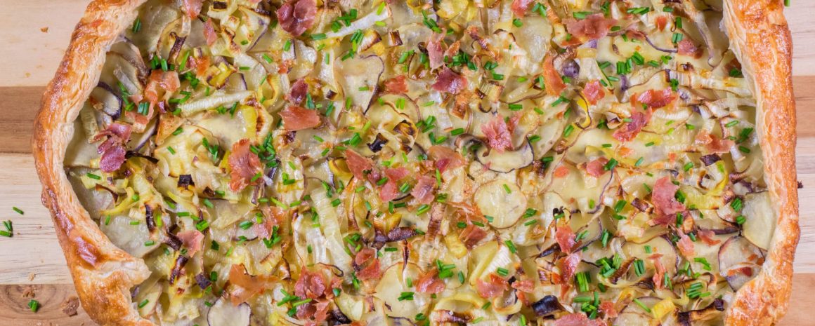 A little potato galette on a cutting board. It looks kind of like a very fancy pizza.