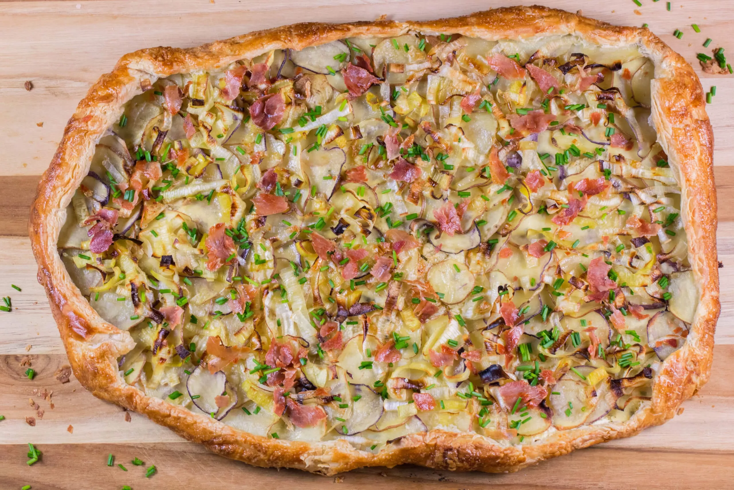 A little potato galette on a cutting board. It looks kind of like a very fancy pizza.