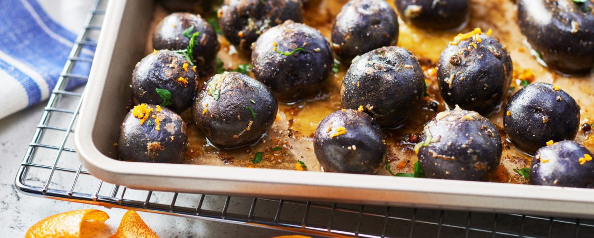 Purple potatoes with some orange zest on a roasting tray.