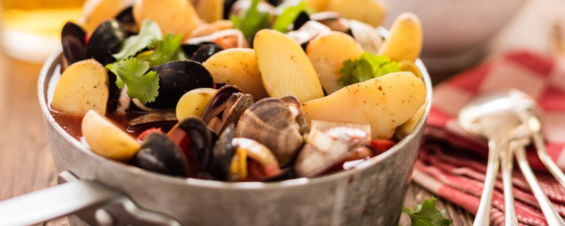 A large stock pot of seafood soup full to bursting with shellfish and potatoes.