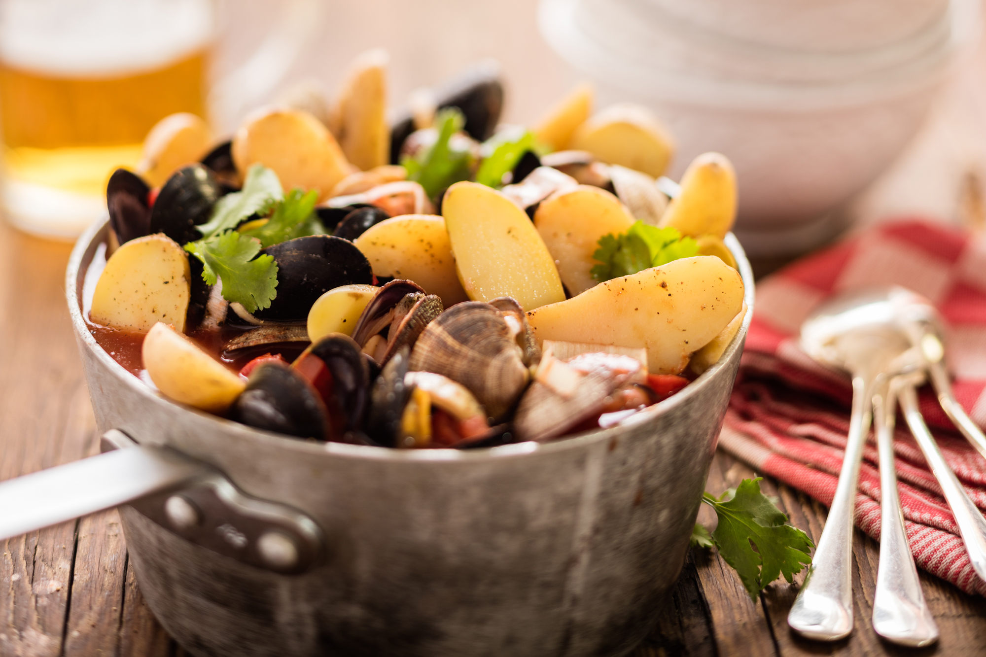 A large stock pot of seafood soup full to bursting with shellfish and potatoes.