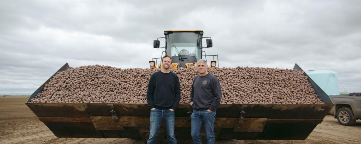 Two of our farmers standing in front of a giant tractor of potatoes.